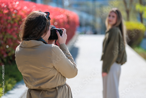 Young woman photographer takes pictures of a model in a park on a sunny day