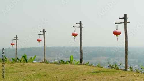 Chinese paper lanterns hang on poles along road in rural Thailand, decorative lanterns fluttering in wind on farm path in northern Thai village, peaceful countryside viewing location for tourists.