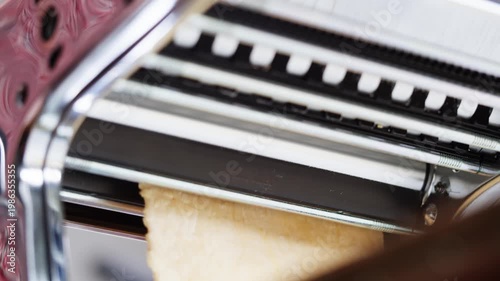 Woman using pasta machine to make fresh pasta dough in the kitchen, cooking in italian restaurant, making noodles.