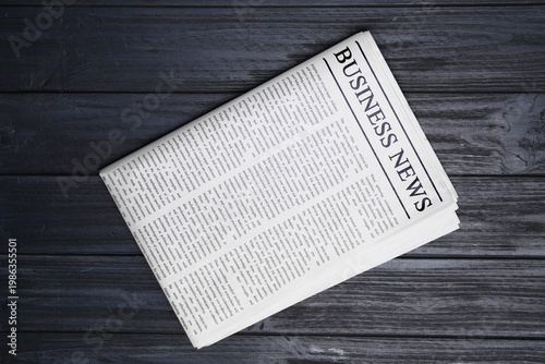 Business newspaper on black wooden background, top view