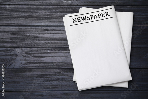 Folded newspapers on black wooden background, top view