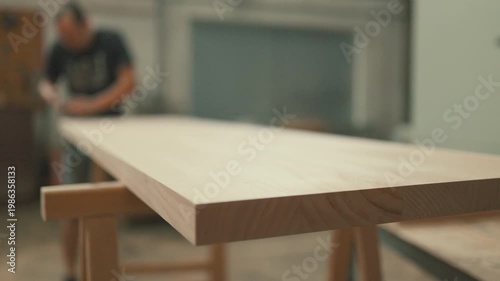 Carpenter sanding a wooden tabletop in a workshop