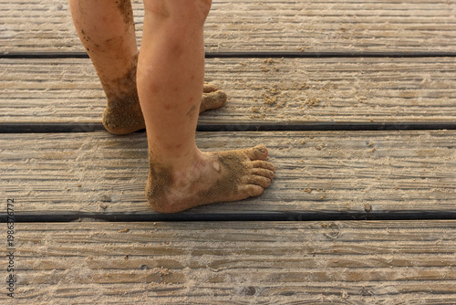 Bare feet of child covered with sand on wooden pier in summer