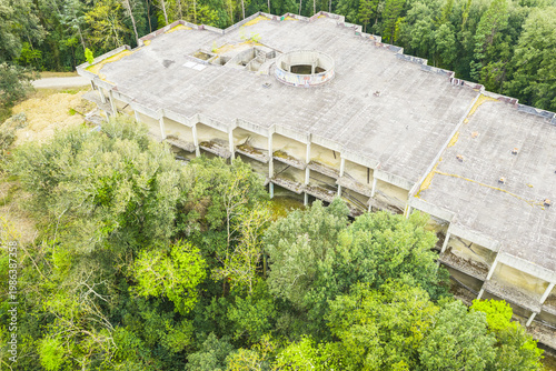 Aerial view of an abandoned modernist concrete building with a flat roof and circular opening surrounded by a dense green forest in Leccio, Toscana, Italy.