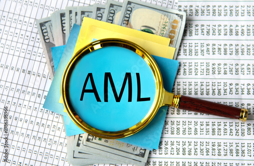 AML - acronym under a magnifying glass against the background of banknotes and tables with numbers
