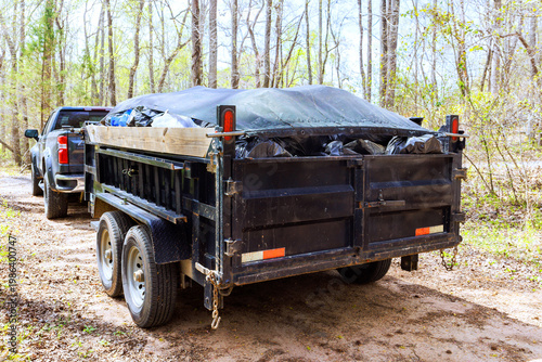 Trailer carries waste materials on dirt road in forested area