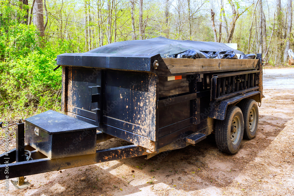 Fototapeta premium Black trailer parked on dirt road surrounded by trees near wooded area