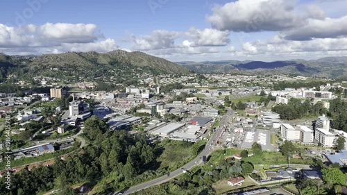 Drone lowers over hill on south side of city with wide shot of downtown in the late afternoon in Mbabane, Eswatini
