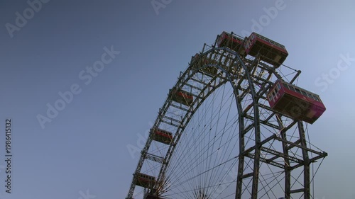 4K low-angle shot of the historic Wiener Riesenrad against a clear twilight sky. The red gondolas of the world's oldest operational ferris wheel rotate in real time, capturing the imperial charm of Au