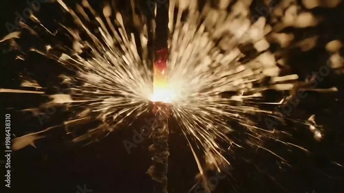 Bright burning festive sparkler emitting glowing golden sparks against a dark black background, close-up view of celebration firework for holidays.