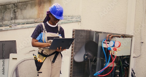 Φωτογραφία Qualified african american electrician working on outside hvac system, holding laptop