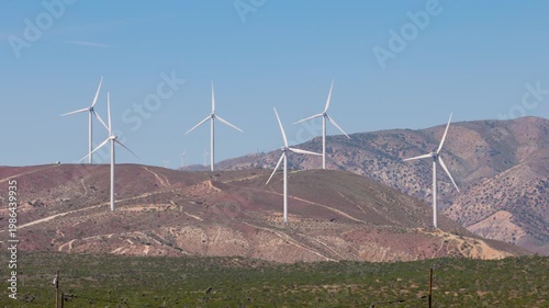 Footage of large white wind turbines generating renewable energy in the desert hills from ground level.