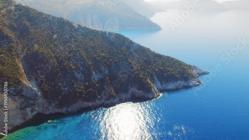 Aerial view of cinematic sunlit green peninsula meeting the Ionian Sea in Greece