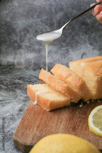 Hand pouring icing glazed on Homemade lemon pound cake on wooden plank. Dessert bakery.
