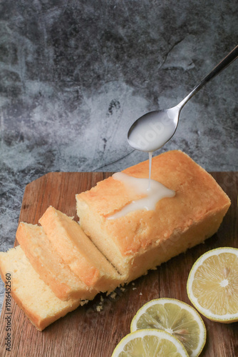 Hand pouring icing glazed on Homemade lemon pound cake on wooden plank. Dessert bakery.