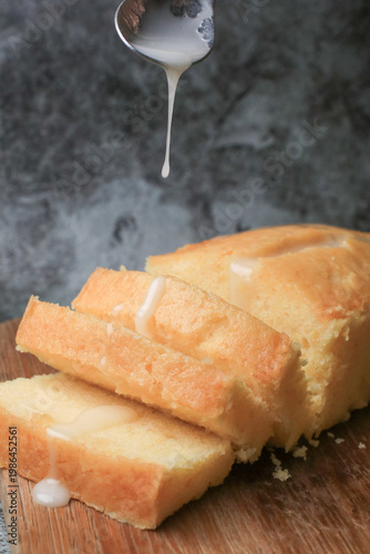 Hand pouring icing glazed on Homemade lemon pound cake on wooden plank. Dessert bakery.