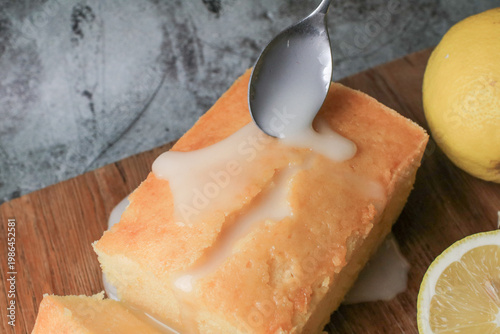 Hand pouring icing glazed on Homemade lemon pound cake on wooden plank. Dessert bakery.