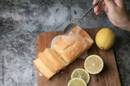 Hand pouring icing glazed on Homemade lemon pound cake on wooden plank. Dessert bakery.