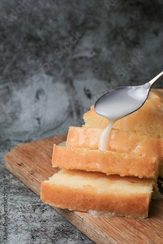 Hand pouring icing glazed on Homemade lemon pound cake on wooden plank. Dessert bakery.