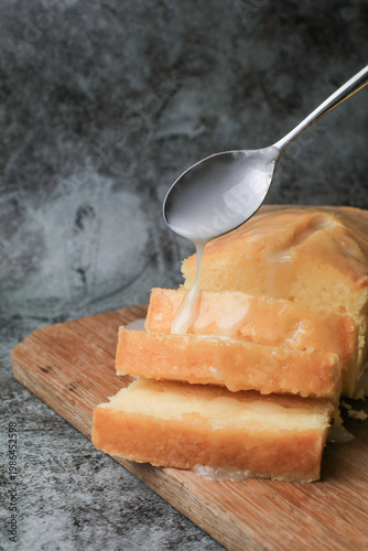 Hand pouring icing glazed on Homemade lemon pound cake on wooden plank. Dessert bakery.