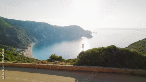 Woman standing on a cliff overlooking a beautiful beach in Kefalonia at sunrise