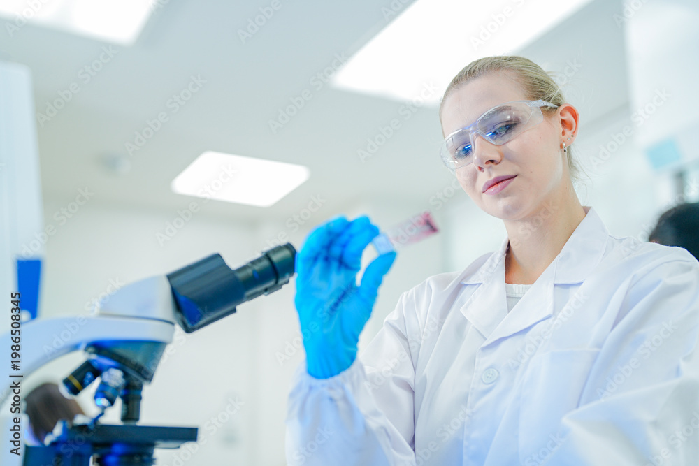 Fototapeta premium Professional female scientist in white lab coat and goggles working with automated laboratory equipment. Expert researcher analyzing clinical samples for biotechnology and medical development.