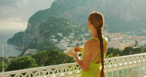 Woman with braid drinking coffee on hotel terrace overlooking Capri Italy coastline in summer