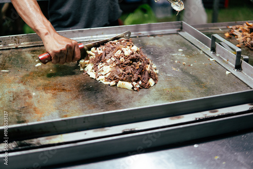 Hand chopping street food meat on griddle