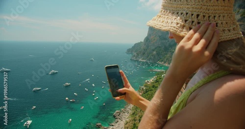 Young woman recording phone video of boats on the blue sea from a sunny viewpoint in Capri