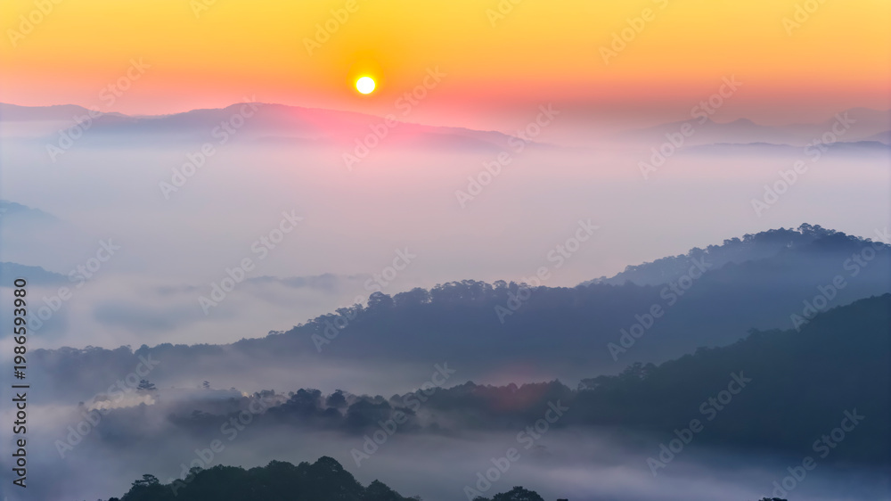 Obraz premium A breathtaking sunrise over a sea of clouds in the highlands, where soft layers of mist drift between rolling hills. The warm glow of the rising sun paints the sky in gentle orange and pink tones
