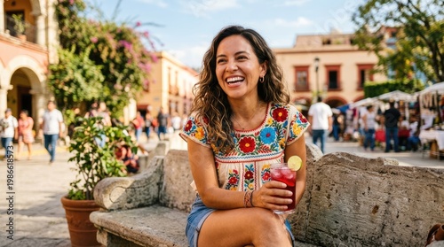 A smiling woman sits on a stone bench in a vibrant Mexican town square.