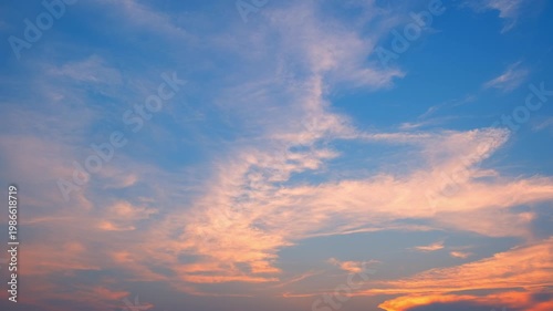 A blue sky timelapse video footage with soft pastel clouds drifting across a clear horizon, blending warm orange and cool blue tones, capturing calm atmospheric motion and natural sky transitions. 4k.