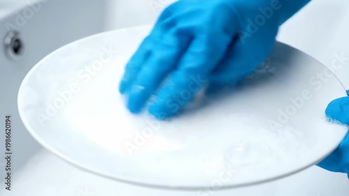 Gloved Hands Washing a Plate with Soap Suds in Kitchen Sink