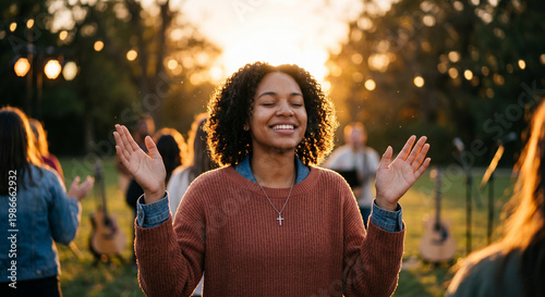 Joyful diverse woman with raised hands during outdoor worship at sunset.