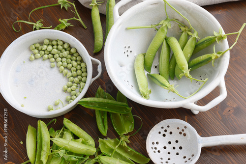 Fresh organic green peas in ceramic bowls on dark wooden table with copy space. High-angle shot features young pea pods and shelled peas highlighting seasonal harvest and healthy farm-to-table