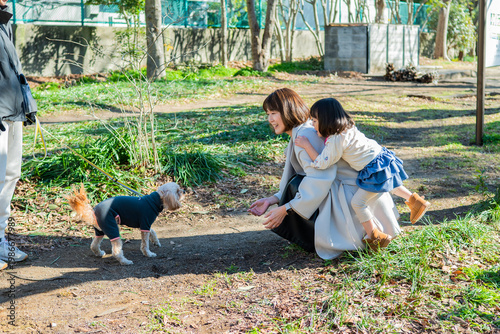 Happy Japanese Mother and Little Daughter Meeting a Small Dog in a Sunny Park
