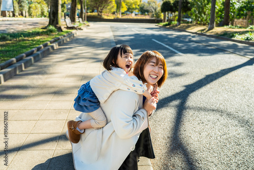 Joyful Japanese Mother and Little Daughter Laughing Together Outdoors in Sunlight