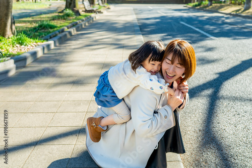 Happy Japanese Mother Carrying Little Daughter Piggyback in Sunny Park