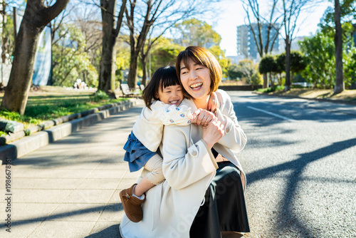 Joyful Japanese Mother and Little Daughter Laughing Together Outdoors in Sunlight