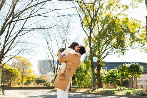 Happy Japanese father lifting his young daughter high in a sunny winter park, family joy