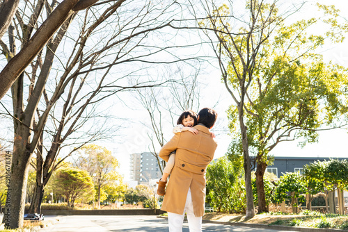 Rear View of a happy toddler girl being carried on her father's back in a public park, family bonding on a sunny winter day