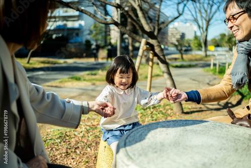 Little girl sitting on a park stool holding hands with both parents, family connection