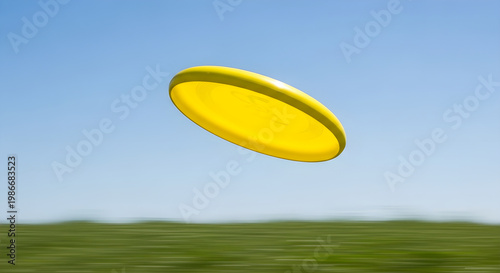 A bright yellow frisbee flies through a clear blue sky over a blurred green field, capturing a moment of outdoor recreation and fun