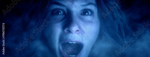 Woman screaming in fear with wild hair against a dark background  