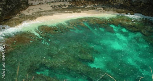 Overhead view of stunning turquoise ocean water waves washing onto narrow white sandy beach with rough rock formation