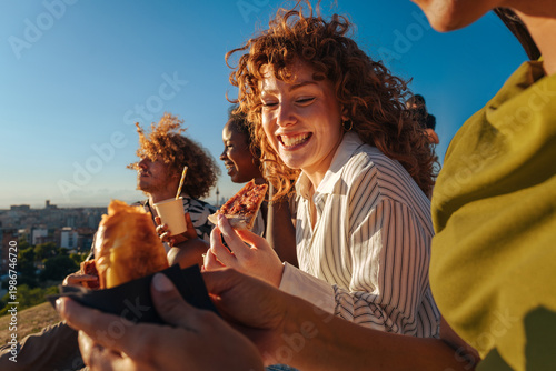 Diverse friends laughing eating pizza outdoors at sunset