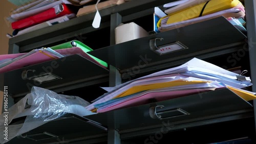 Stacks of paper files and folders cluttered on metal shelves in a poorly maintained medical facility in Cameroon. Close-up view.