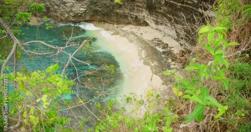 Scenic view small crescent white sand beach and turquoise water at bottom of steep cliff in Nusa Penida
