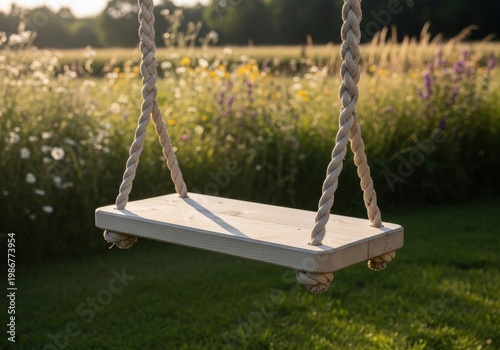 A wooden swing hangs from ropes in a field of flowers