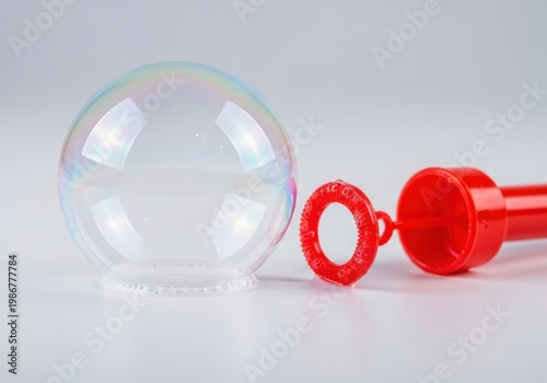 A large bubble and a red bubble wand on a white surface